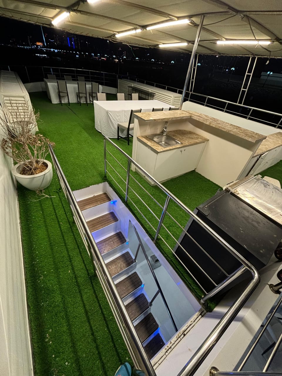 Lit stairway leading up to the open top deck with tables and city lights beyond